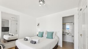 A modern bedroom with a large bed, a mirror, and a view into the bathroom. - Apartamento Mar Azul (Puerto del Carmen)