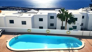 A swimming pool with a clear view of the sea and a building with white walls and multiple windows. - Apartamento Mar Azul (Puerto del Carmen)