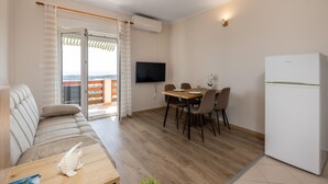 A modern living room with a sofa, a dining table with chairs, a flat-screen TV, and a refrigerator. - Beautiful apartment in Palit with WiFi (Palit)
