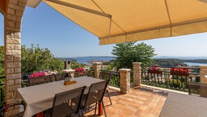 A terrace with a table and chairs, a stone wall, and a view of the sea and landscape. - Beautiful apartment in Palit with WiFi (Palit)