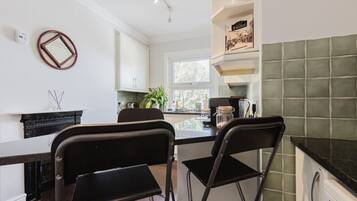 A modern kitchen with white cabinets, a black countertop, and a green tiled backsplash. There are two black chairs and a window providing natural light.