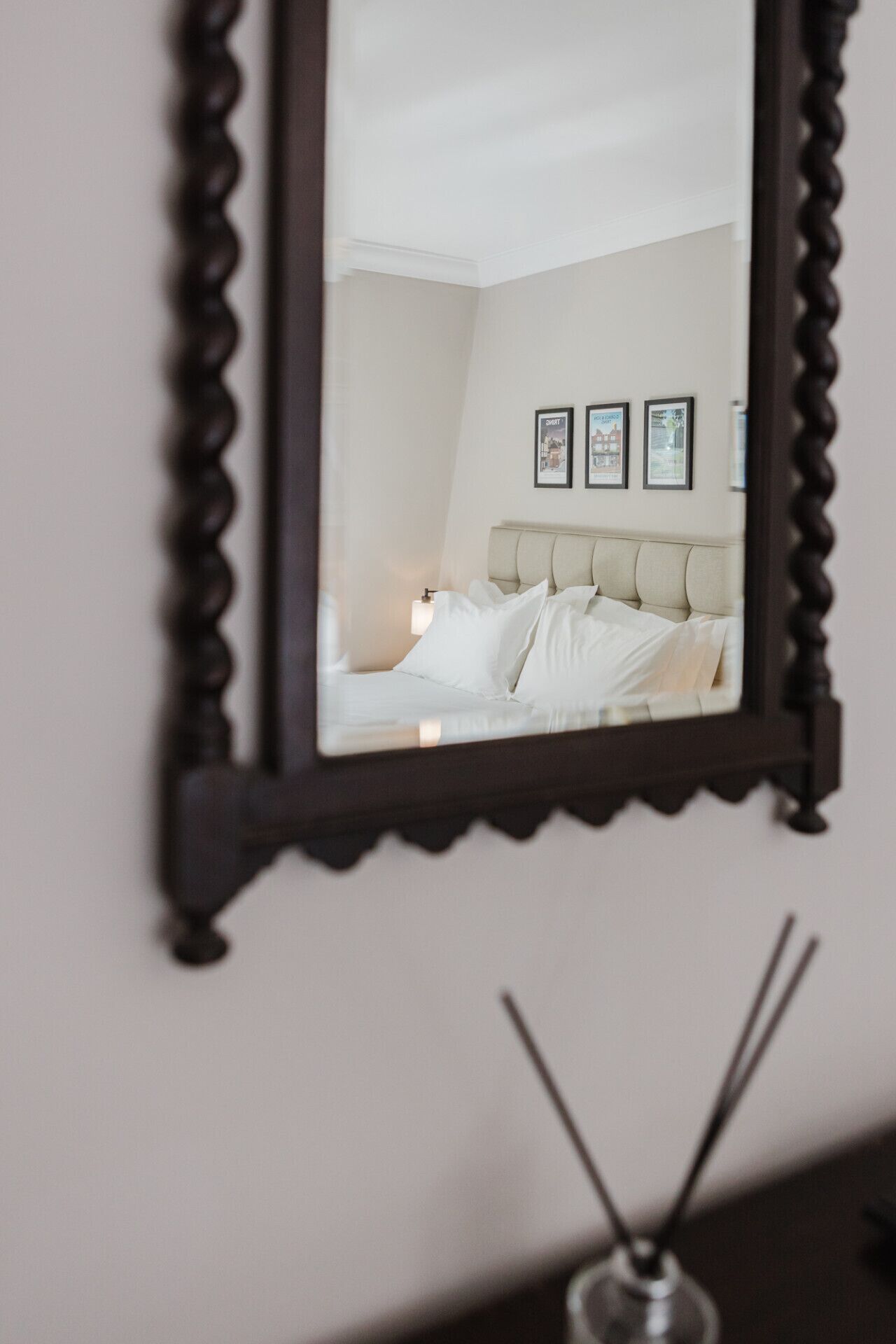 A bedroom with a bed, a bedside table, a mirror, and three framed pictures on the wall.