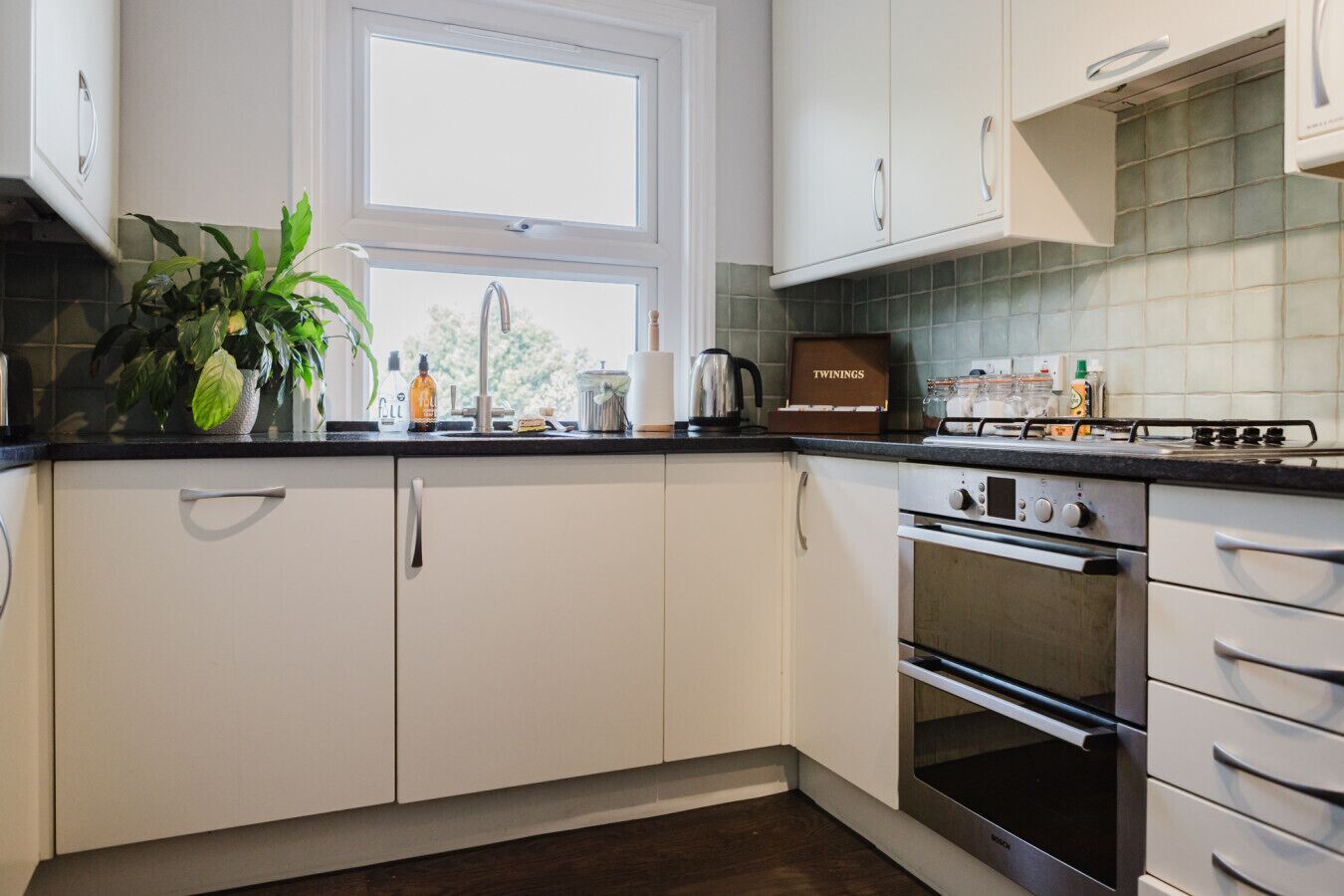 Eine moderne Küche mit weißen Schränken, einem Gasherd, einem Backofen und einem Fenster über der Spüle.