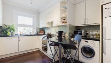 A modern kitchen with white cabinets, a black countertop, a sink, a stove, a microwave, a washing machine, and a window providing natural light.