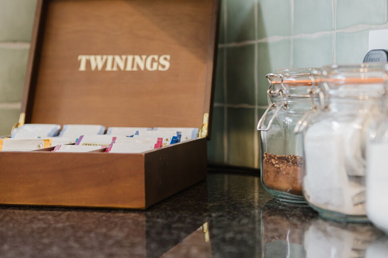 Eine Schachtel mit dem Aufdruck "TWININGS", diverse Gegenstände und ein Glasbehälter mit Metalldeckel auf einer Arbeitsplatte.