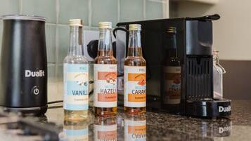 Eine Küchenarbeitsplatte mit verschiedenen Gegenständen, darunter ein Dualit Staubsauger, Flaschen mit M&S Aroma-Sirup und eine Kaffeemaschine.