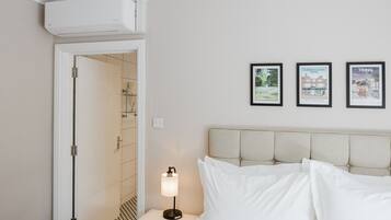 Une chambre d’hôtel avec un lit, une table de chevet avec une lampe, une porte donnant sur une salle de bain et trois tableaux encadrés accrochés au mur.