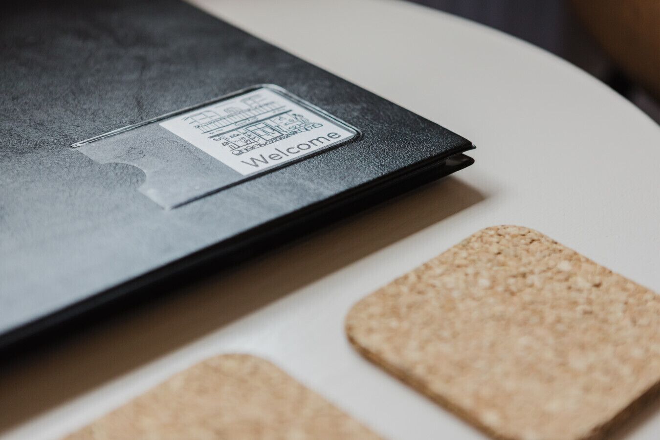 A black folder with a welcome sticker on a white surface with cork tiles.