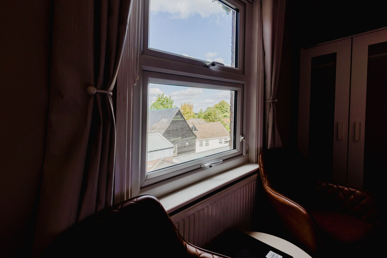 A room with a window overlooking a residential area, a radiator below the window, and a chair to the right.
