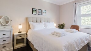 A neatly arranged bedroom with a large bed, a bedside table with a lamp, a dresser, and a window with curtains. - Grace`s Guesthouse Room 3 (Tring)