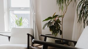 Quarto com poltrona branca, mesa redonda com duas fatias de pão e um vaso de planta.