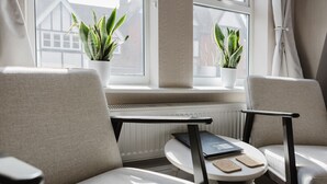 Uma área de estar aconchegante com duas cadeiras e uma pequena mesa, um laptop e um livro. Há duas plantas em vasos no parapeito da janela.