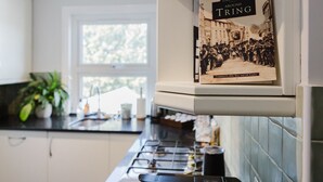 Cozinha com armários brancos, uma janela e um livro chamado 'Around Tring' em uma estante.