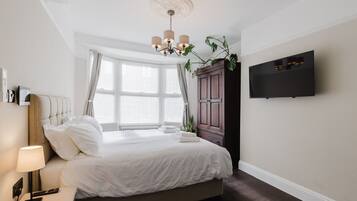 Une chambre d’hôtel avec un lit, une table de chevet, une lampe, une télévision et une grande fenêtre avec des rideaux.