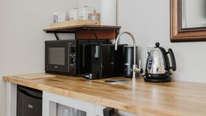 A kitchenette with a microwave, coffee maker, kettle, and a shelf with containers labeled sugar and coffee. - Grace`s Guesthouse Room 5 (Tring)