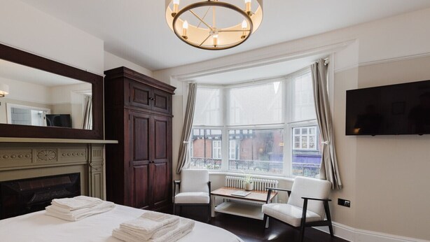 A hotel room with a large bed, a fireplace, a bay window with curtains, a television, and a desk with a chair. - Grace`s Guesthouse 68b (Tring)