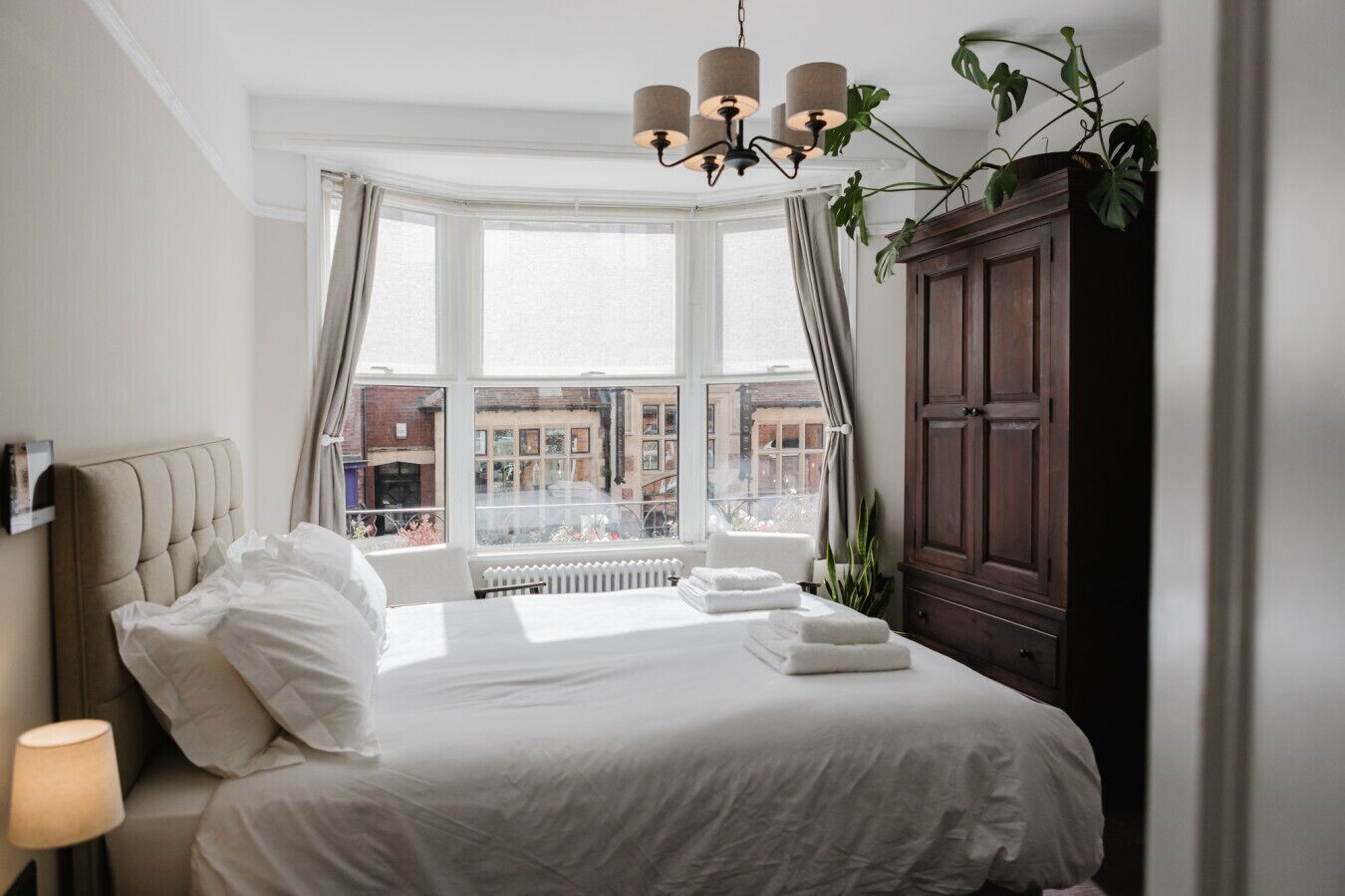 Una camera da letto con un letto grande, una finestra con tende, un armadio in legno e un lampadario.