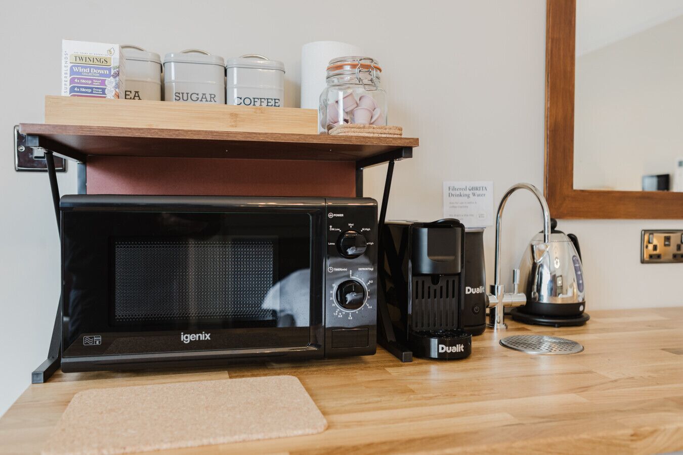 Una kitchenette con microondas, cafetera y frascos de almacenamiento etiquetados 'azúcar' y 'café'.