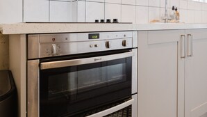 Een keuken met een roestvrijstalen oven, een digitale klok waarop 15:59 staat, en witte kasten.