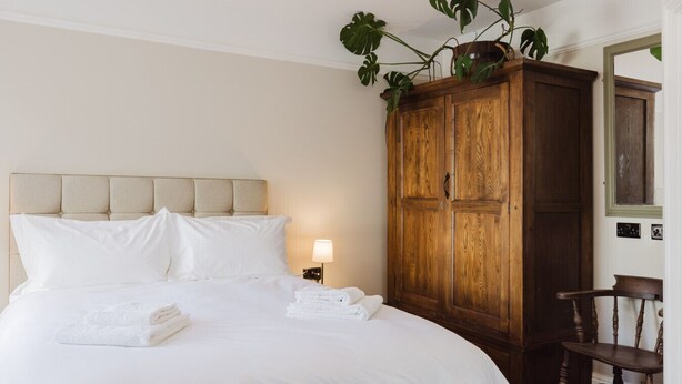 Een netjes opgemaakt bed met witte lakens en handdoeken, een houten garderobe en een stoel.