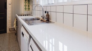 Een keuken met witte tegels, een spoelbak, een kraan en een raam.