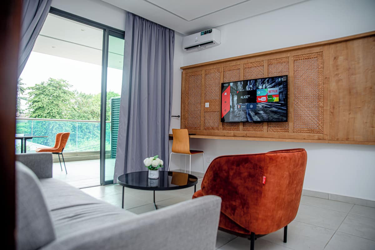 A modern living room with a sofa, a red chair, a small table with a vase, and a TV mounted on a wooden panel.