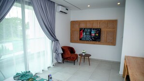 Moderni hotellihuone, jossa on suuri ikkuna, seinälle asennettu litteänäyttöinen televisio, punottu koristepaneeli, puinen ruokapöytä ja viihtyisä oleskelualue, jossa on nojatuoli.