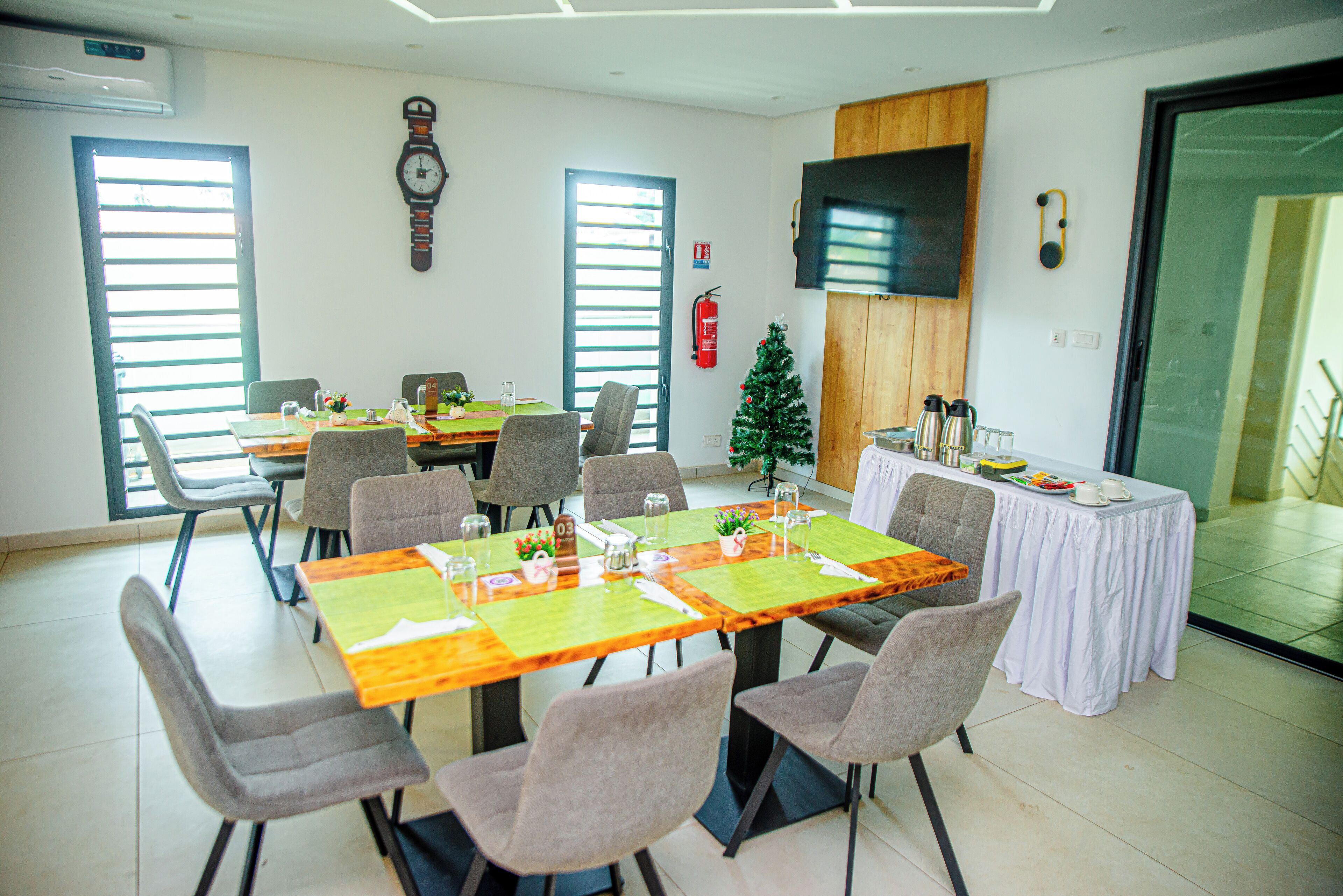 Een vergaderzaal met een lange tafel, meerdere stoelen, een kleine kerstboom en een brandblusser aan de muur.
