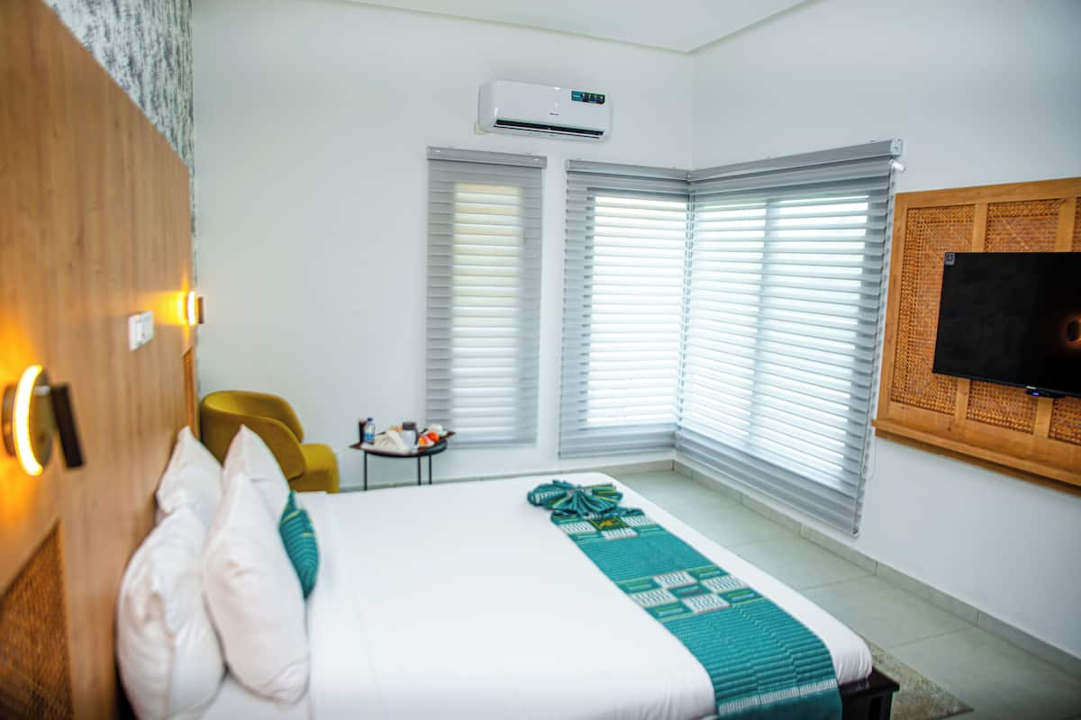 A hotel room with a bed, a small table with a lamp, a chair, and a TV mounted on the wall.