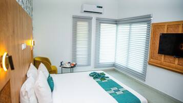 Una habitación de hotel con una cama, una mesita con una lámpara, una silla y un televisor en la pared.