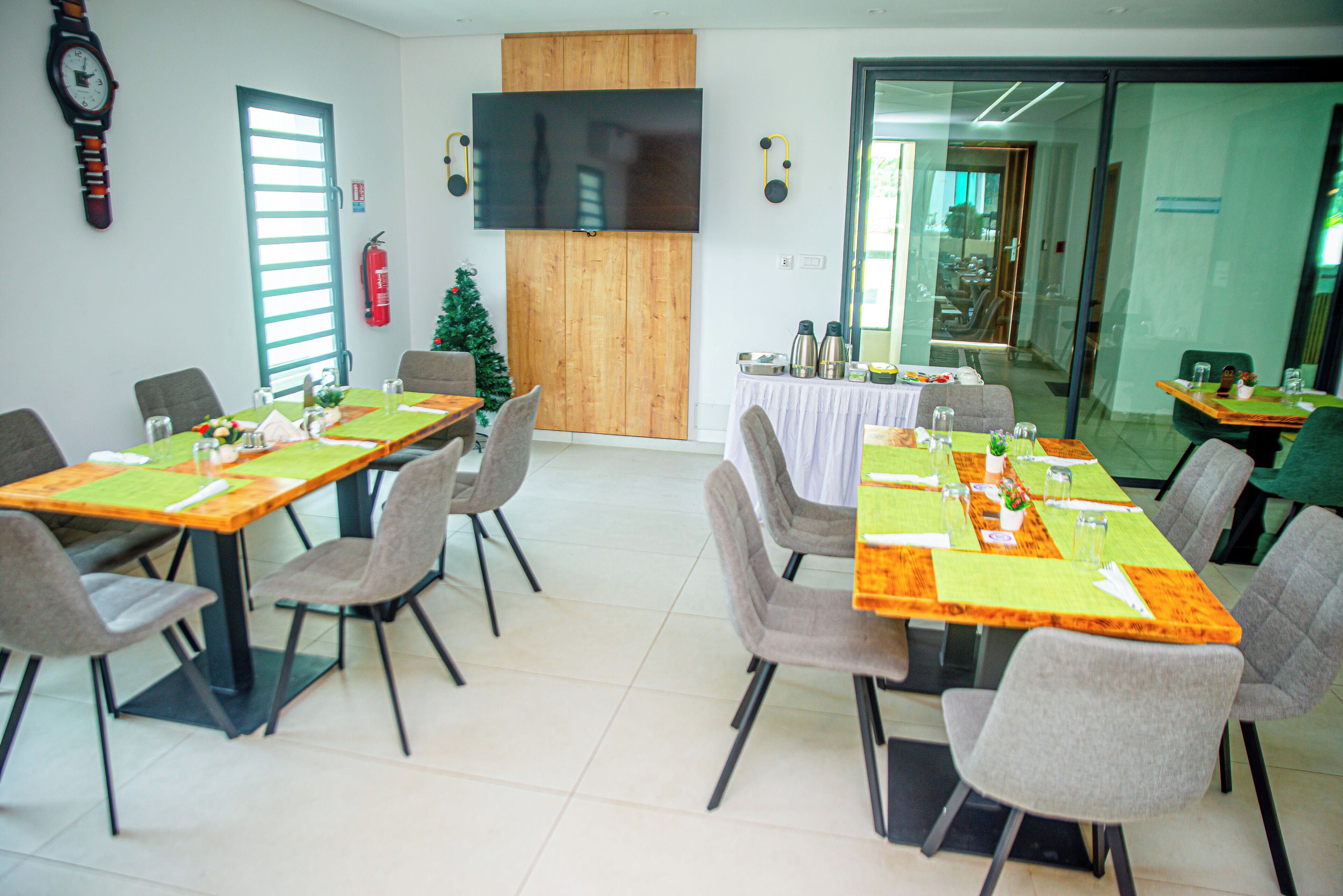 Une salle de conférence avec deux longues tables, des chaises grises, un mur décoratif en bois, un téléviseur à écran plat et un sapin de Noël.