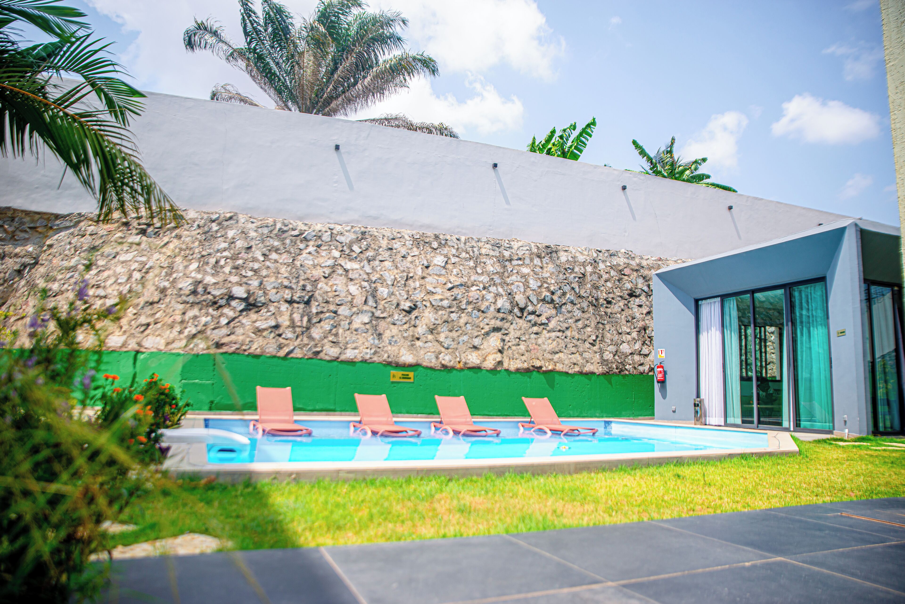 A modern hotel with a swimming pool, lounge chairs, and a stone wall.