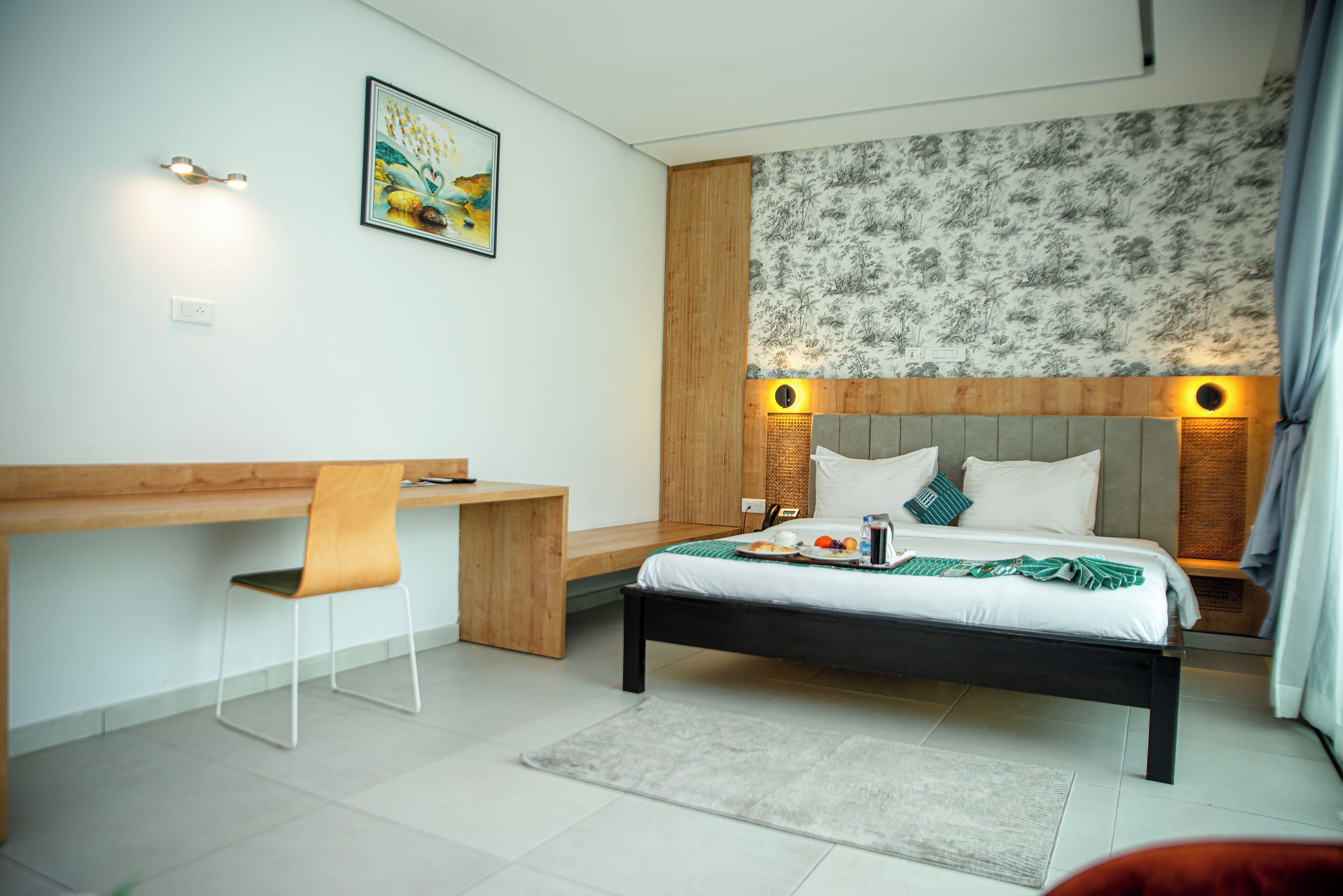 A modern bedroom with a wooden desk, a bed with a headboard, and a wall-mounted light fixture.