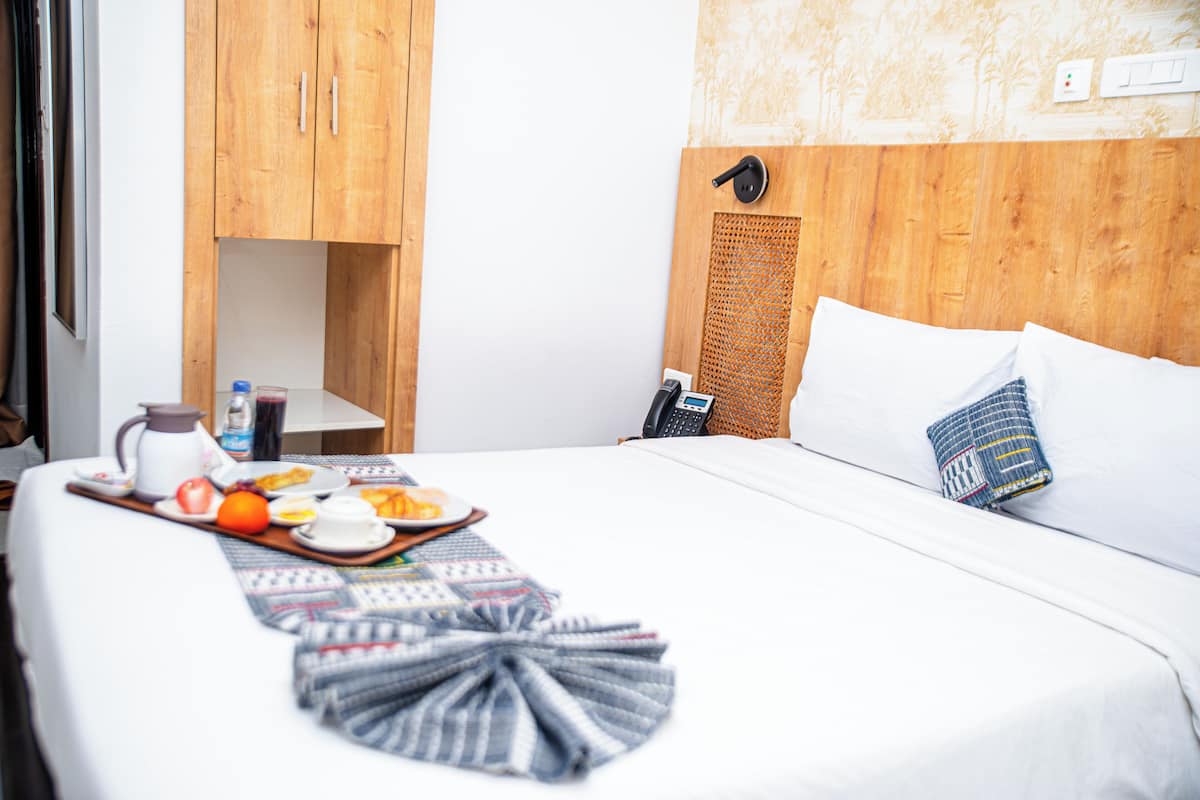 A hotel room with a bed, a wooden wardrobe, a small table with breakfast items, and a wall-mounted phone.