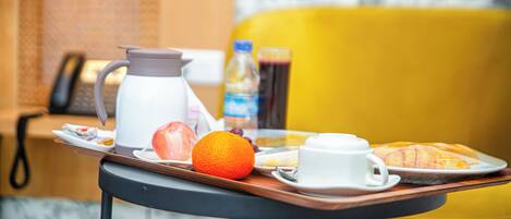 A breakfast tray with orange juice, croissant, and coffee on a table in a room with a yellow chair and a telephone.