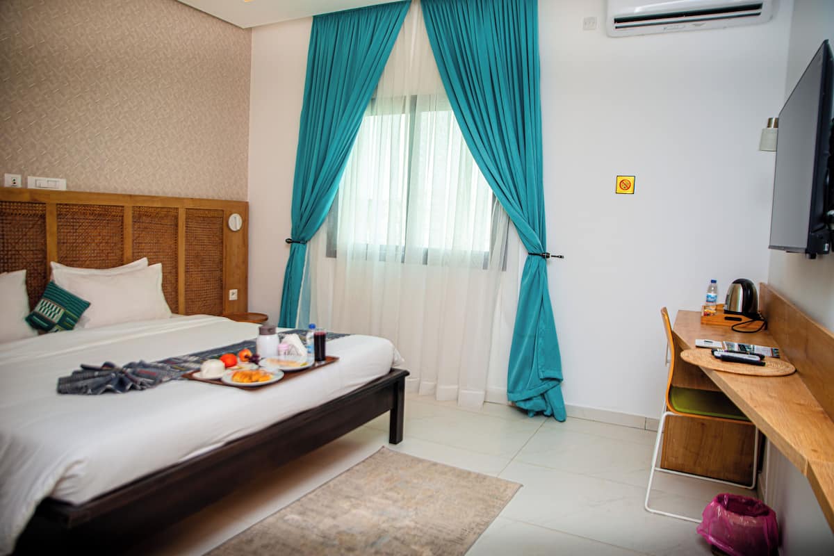 A hotel room with a bed, a desk, and a window with curtains.