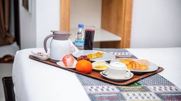 Una bandeja de desayuno ordenada sobre una cama, con jarra, botella de agua, jugo, fruta y un croissant.