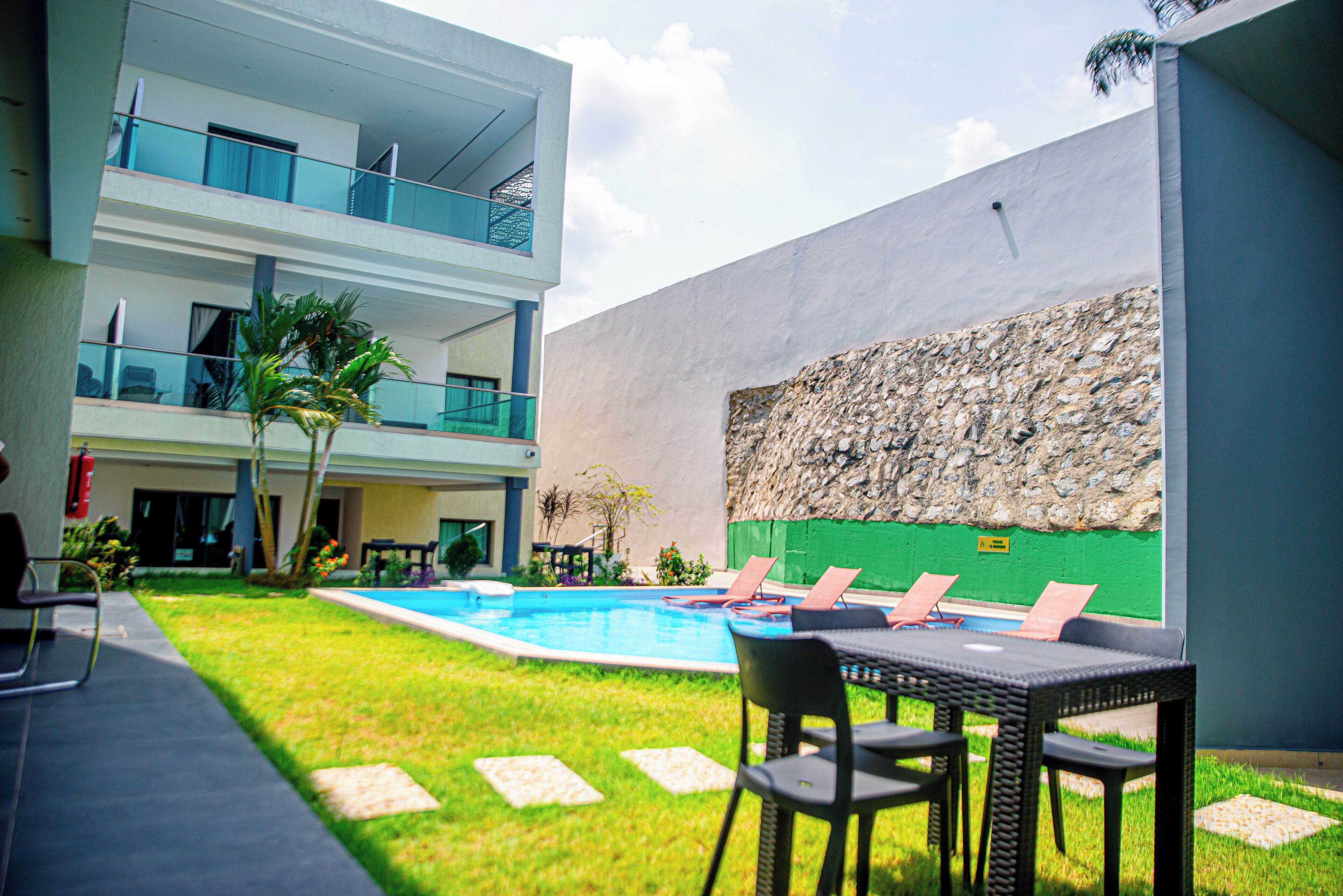 Un edificio moderno con piscina, mobiliario exterior y un muro de piedra.
