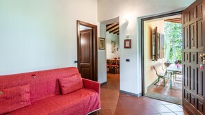 Un sofà vermell en un passadís amb una porta de fusta i vista cap a una zona de menjador.