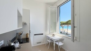 A compact kitchen with a dining area, a large window with a beach view, and a white color scheme.
