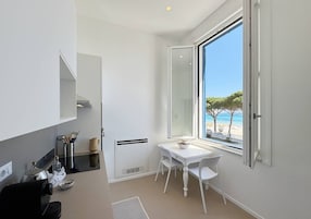 Una cocina compacta con comedor, un ventanal con vista a la playa y una decoración en tonos blancos.