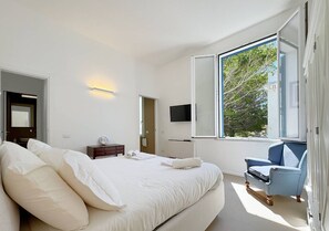 A modern bedroom with a large bed, a TV mounted on the wall, and a window with a view of trees. - Solemar Sicilia - Villa Regina Elena (Palermo)