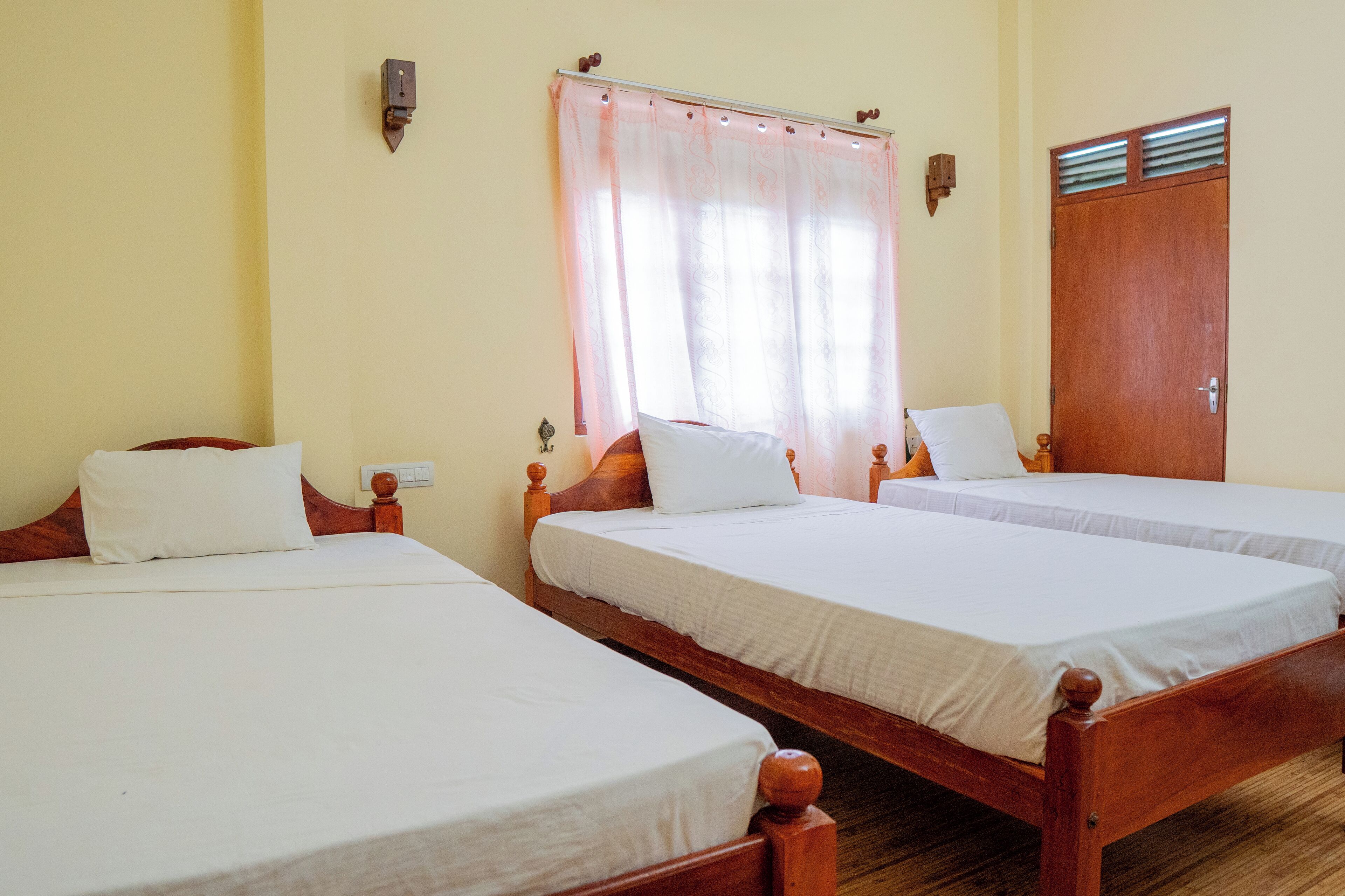 A hotel room with three wooden beds, each with white linens and wooden headboards.