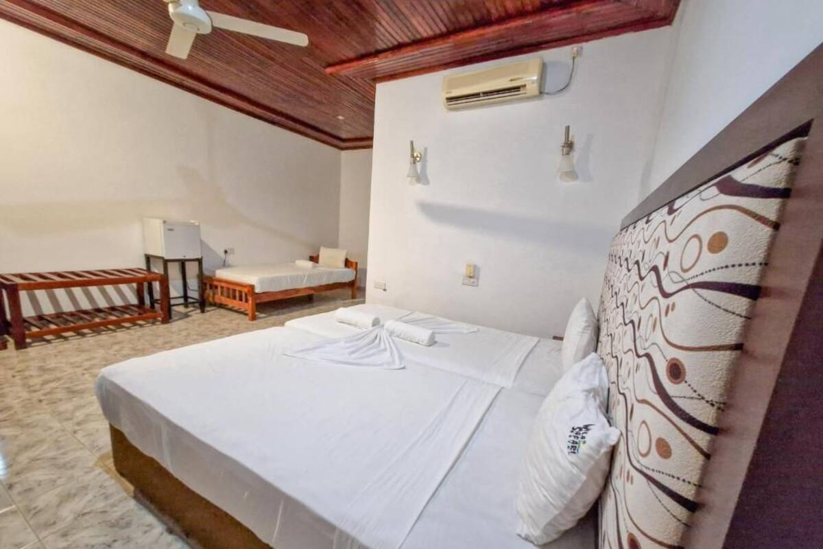 A hotel room with a large bed, a small desk, a chair, and a ceiling fan.