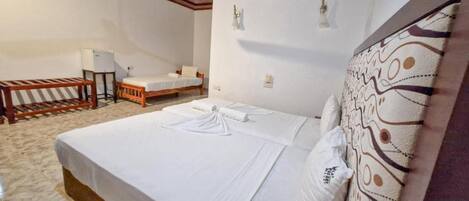A hotel room with a large bed, a small desk, a chair, and a ceiling fan.