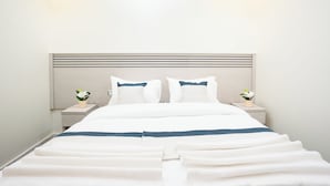 Una cama bien hecha con ropa de cama blanca y azul, dos mesitas de noche con lámparas y un aplique de pared.