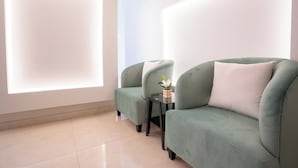 Una habitación moderna con dos sofás verdes, una mesita con un jarrón de flores y un ventanal que deja entrar mucha luz natural.