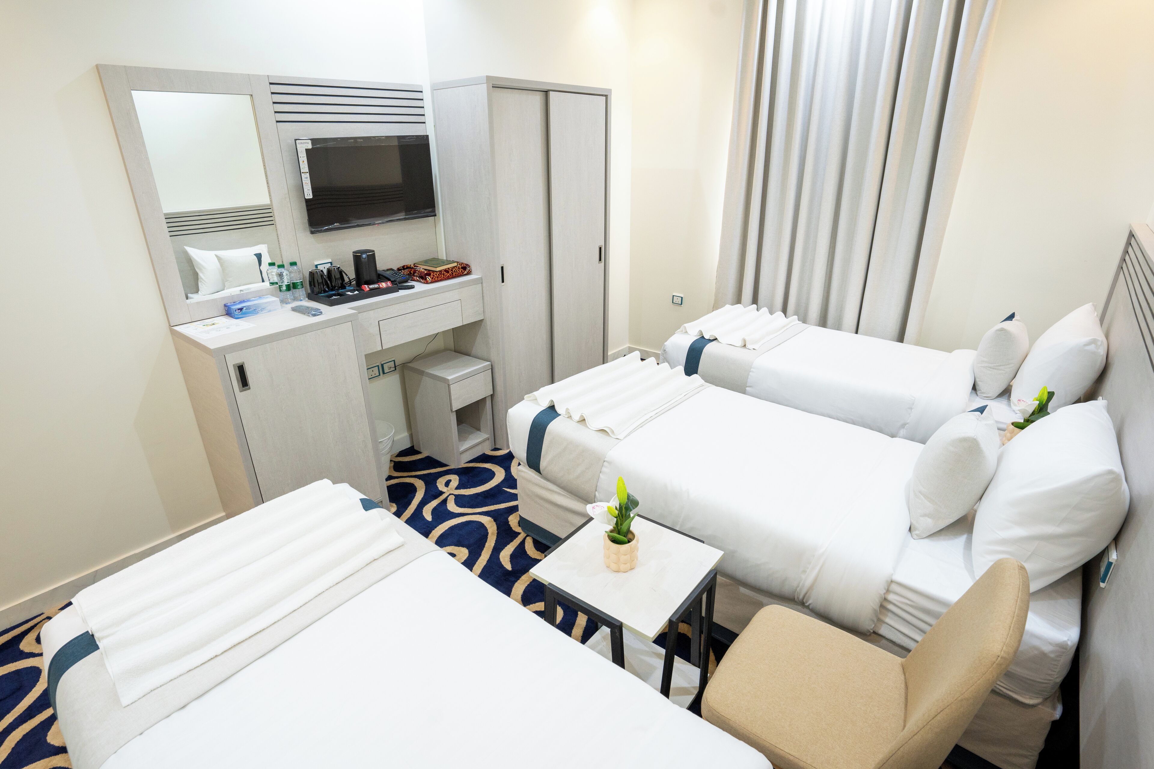 Ein Hotelzimmer mit zwei Betten, einem Schreibtisch, einem Stuhl, einem kleinen Tisch, einem Fernseher und einem Kleiderschrank.