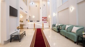 Un moderno vestíbulo de hotel con un mostrador de recepción, zona de estar y una alfombra roja que conduce a la entrada.