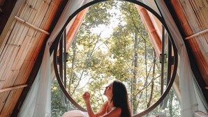 A cozy bedroom with a large circular window, a bed with white linens, and a wooden ceiling structure. - Lannawild Chiang Mai (Mae On)